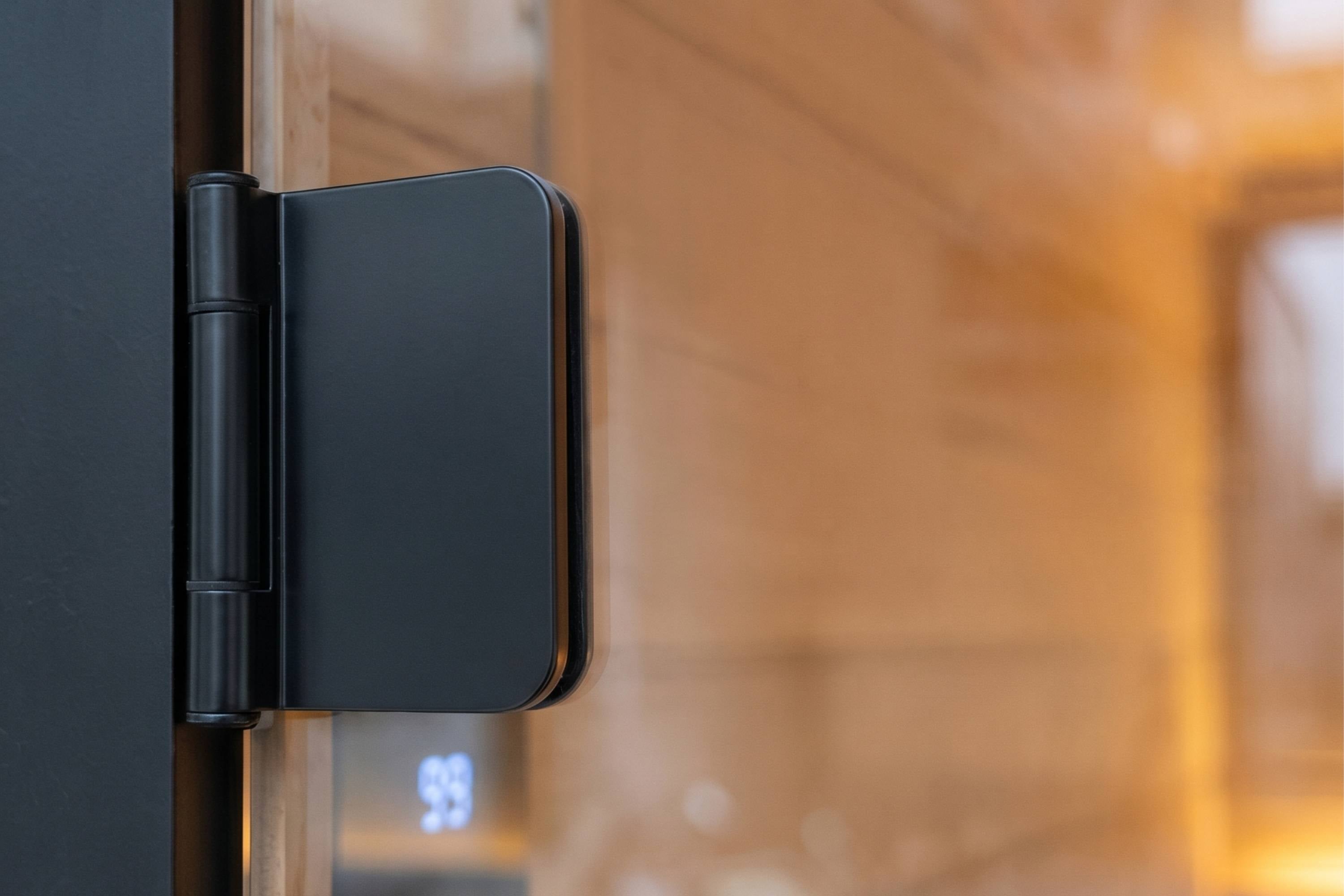 Close-up of black glass sauna door hinge on Swell Black Eco 4 outdoor sauna